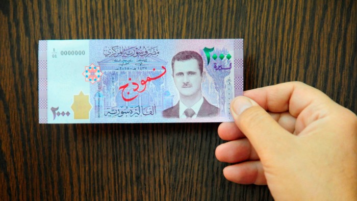 A person holding a 2,000 Syrian pound bill