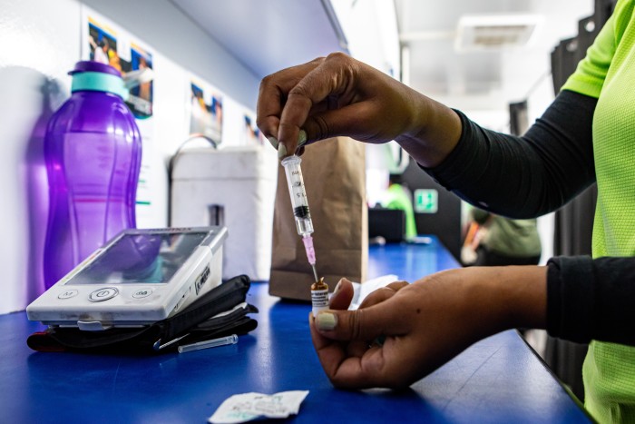 A healthcare worker in a lime-green shirt prepares a syringe with medicine inside a mobile clinic