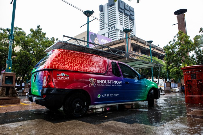 A large, brightly coloured mobile health clinic with “SHOUT-IT-NOW” branding on the road in Pretoria, South Africa