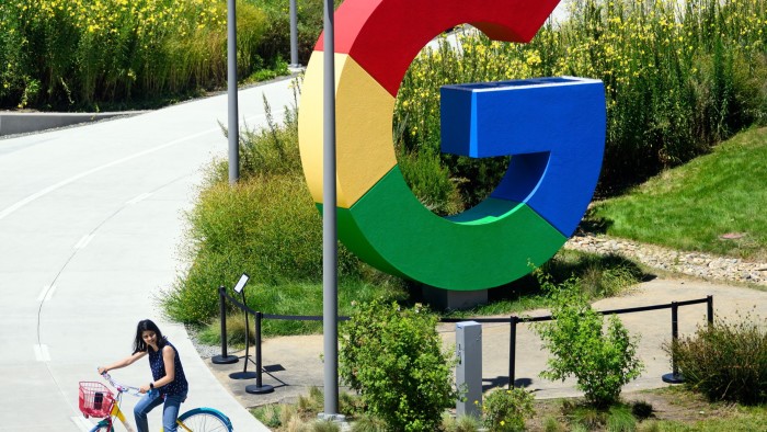 A person rides a bicycle past a Google logo