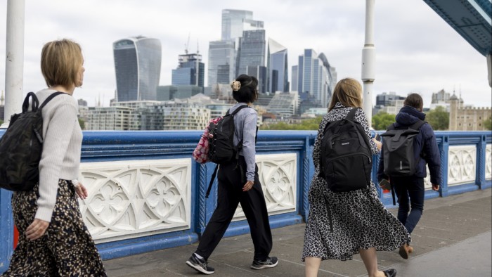 Commuters cross Tower Bridge with skyscrapers in the City of London in the background