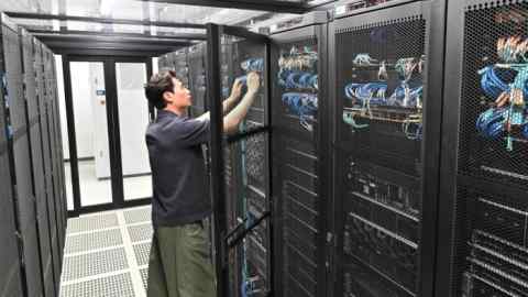 A man in a blue short-sleeved shirt has opened a tech cage and is fiddling with some blue wires