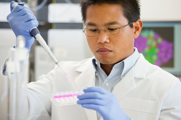 A pharmaceutical lab technician using a pipette device to place liquid into a sample tray.