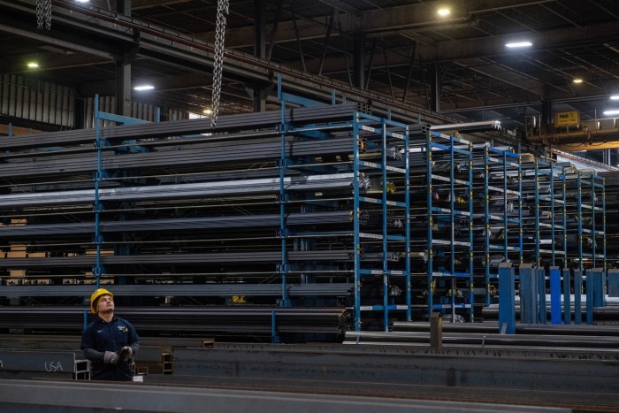 A worker moves a crane to lift a steel beam at a company in Massachusetts