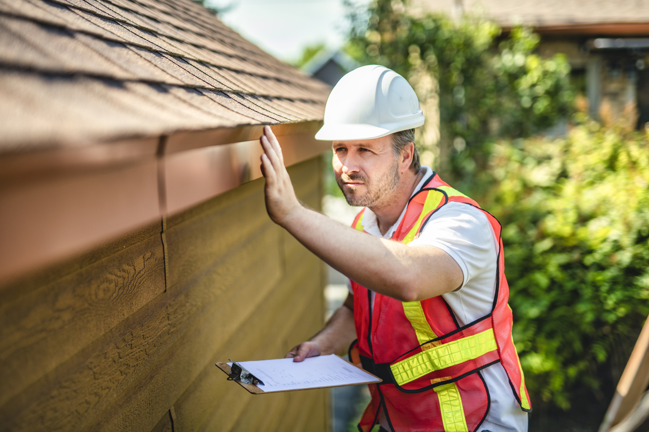 Man is inspecting roof with a clipboard in his hands.