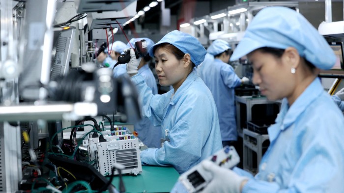 Workers in blue uniforms and caps operate on a production line at an automotive navigation product  factory in Jiangsu province, China