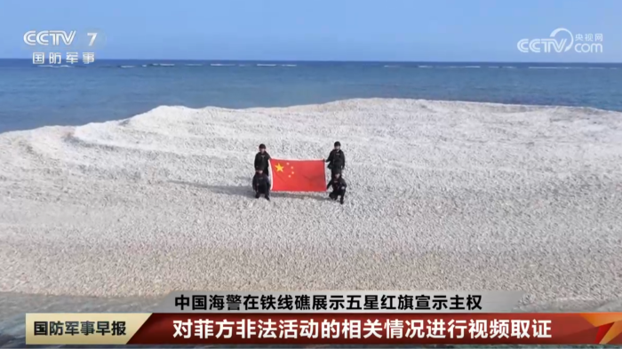 Four figures in uniform hold a Chinese national flag on a sandbank in a screengrab from CCTV