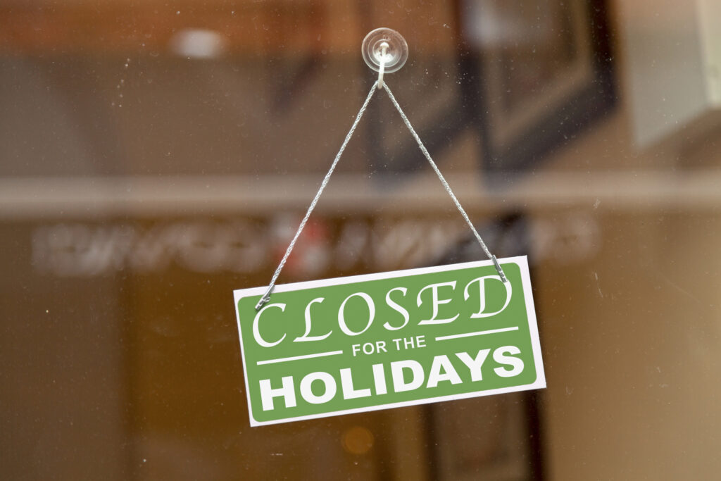 Green sign hanging at the glass door of a shop with written in it &quot;Closed for the holidays&quot;.