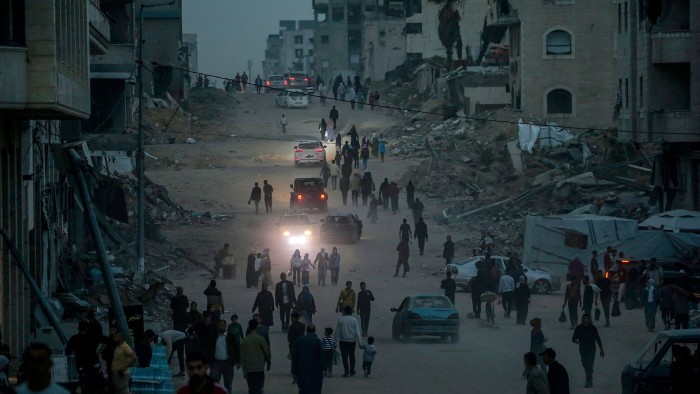 Palestinians walk along a dusty street lined with debris and destroyed buildings in Gaza City