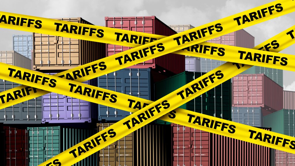 Shipping containers in the background are crisscrossed with yellow tape that says tariffs.