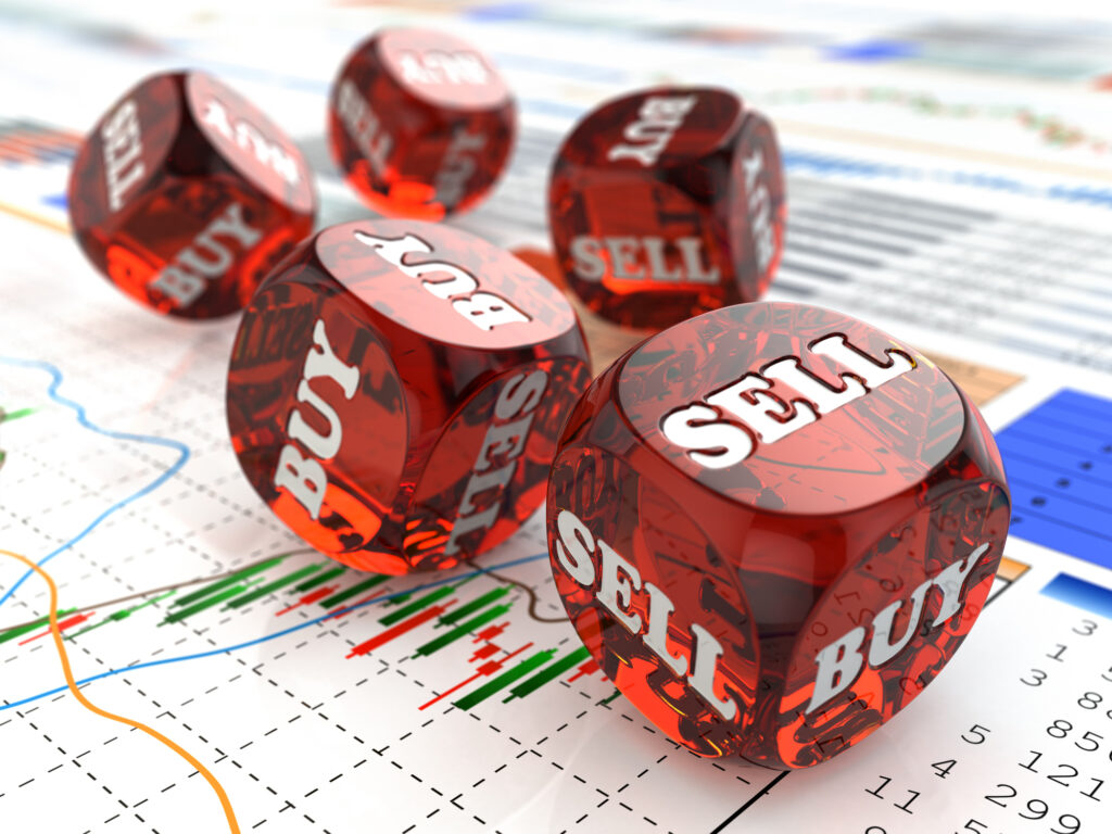red dice with the words "sell" and "buy" written on them sitting on financial charts