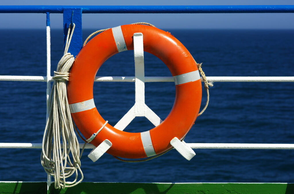 Ship railing and red life ring foreground, blue sea background