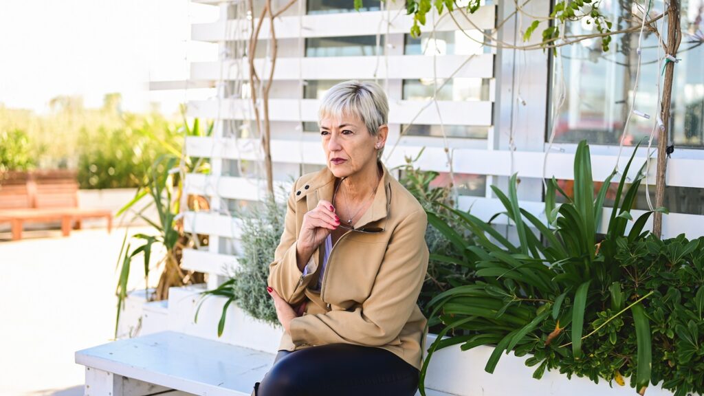 A senior woman sits on a bench outside.