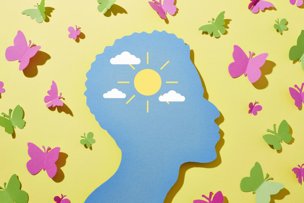 yellow background with pink and green paper butterflies and a blue profile of a person with a yellow sun in the head