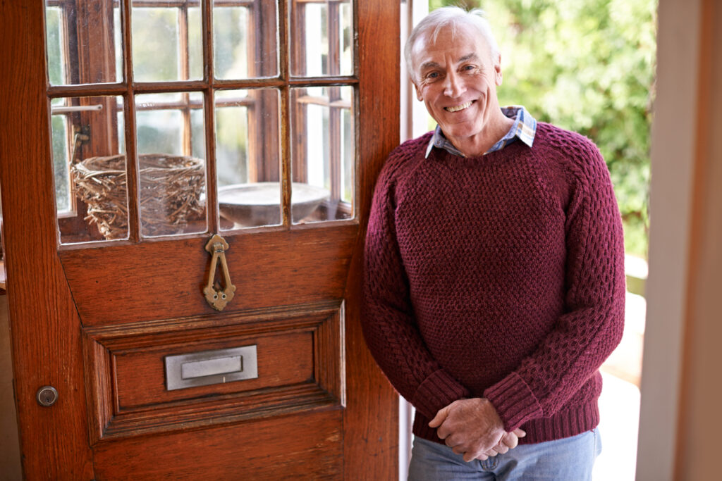 An older, fit man stands in the doorway to his home or rental home.