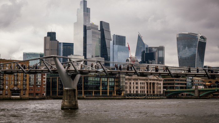 Commuters cross Millennium Bridge in view of the skyline of the City of London