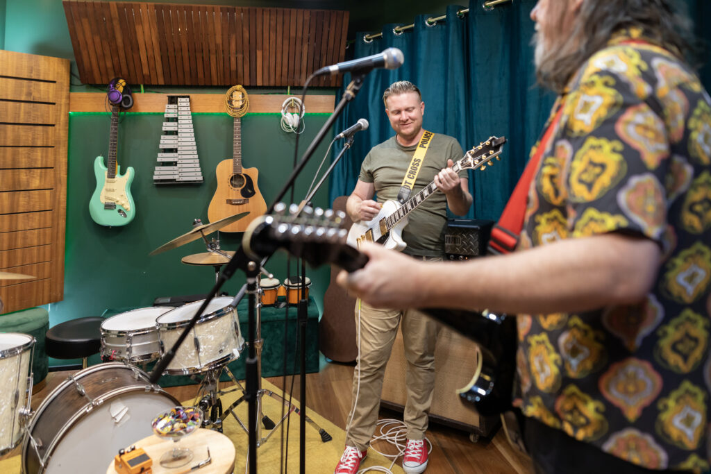 Two retired men play guitar in a basement studio.