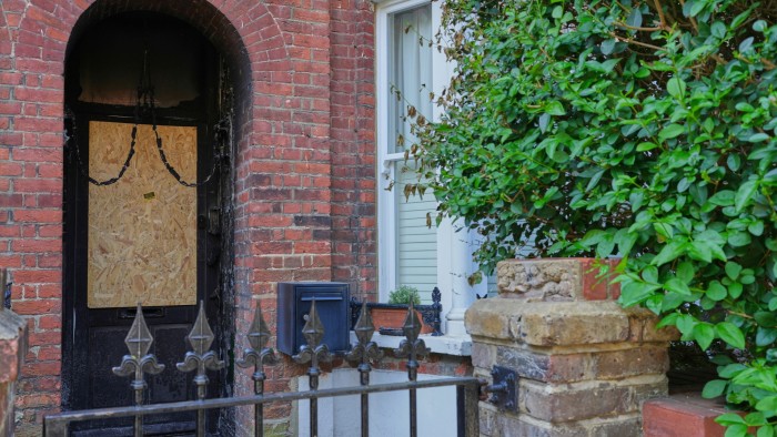 A boarded-up doorway shows signs of fire damage, with scorch marks visible around the entrance