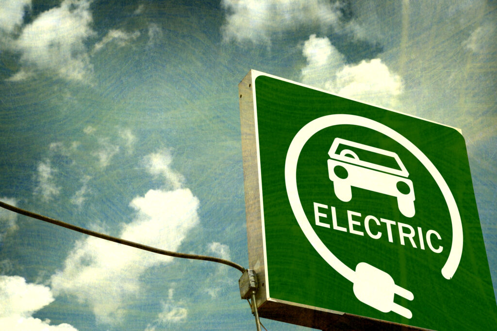 aged and worn photo of an electric vehicle sign against the sky