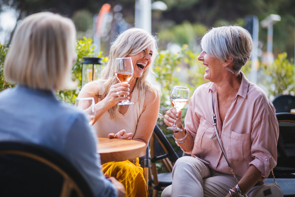 Two woman laughing while drinking wine outdoors