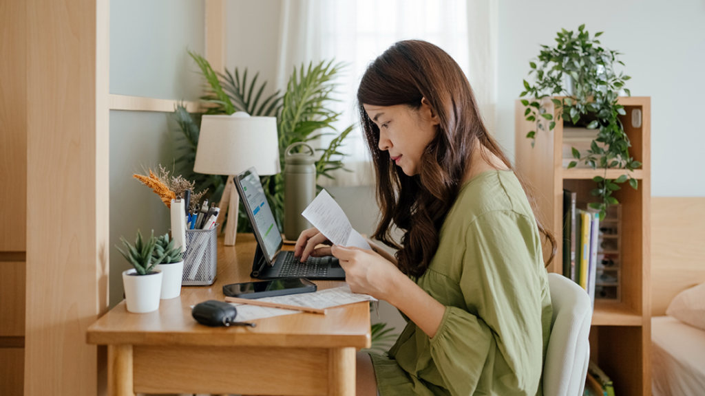 A woman at a desk looking over paperwork with a laptop