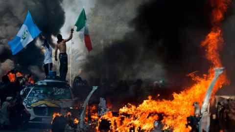 Protesters wave flags as burning cars line the street