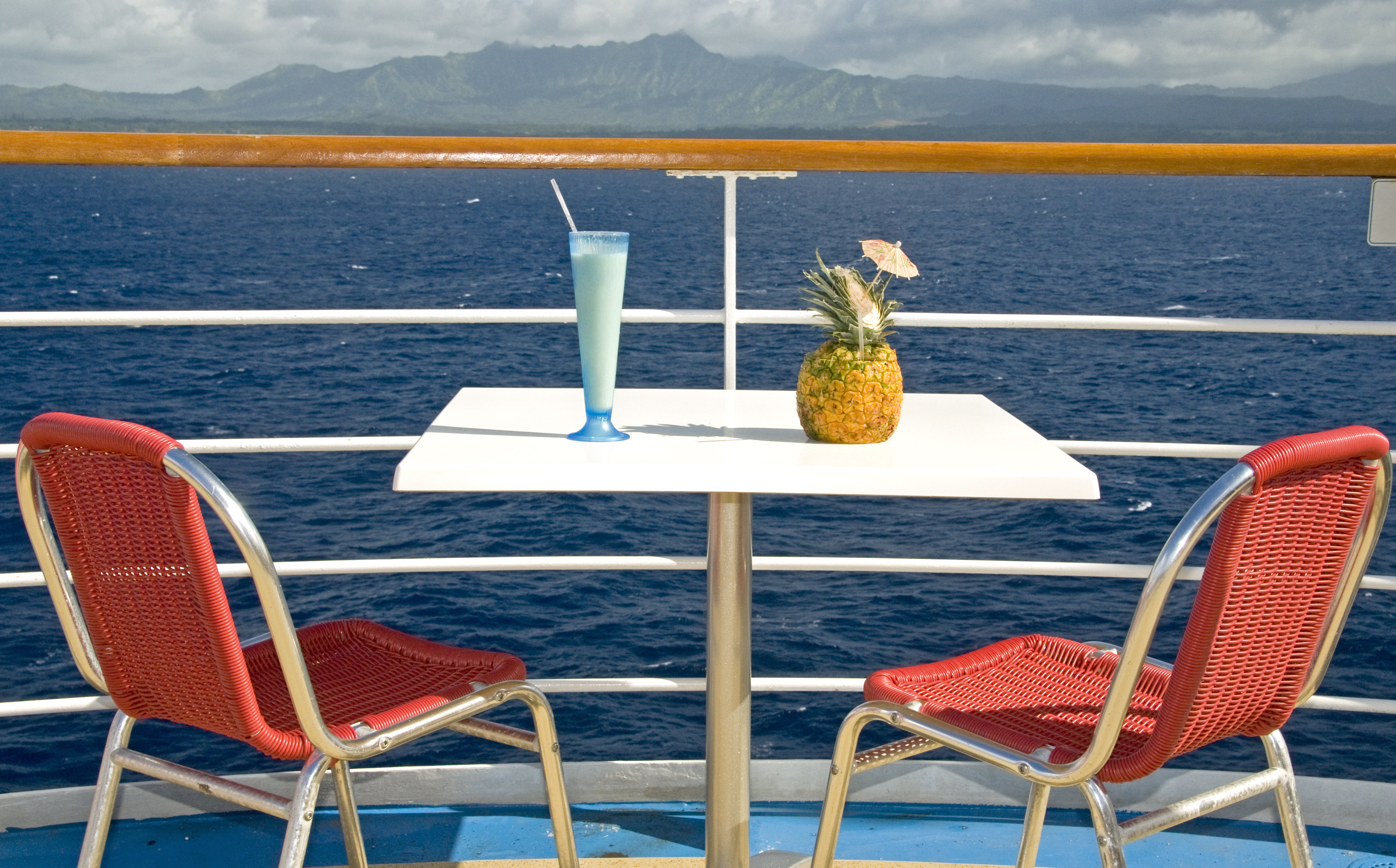 Red chairs on a boat deck overlooking the ocean in Hawaii with fancy beverages.