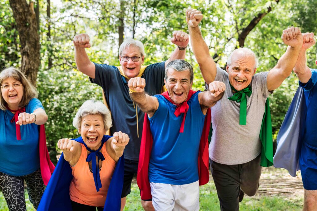 A group of older adults wearing super hero capes with their fists in the air