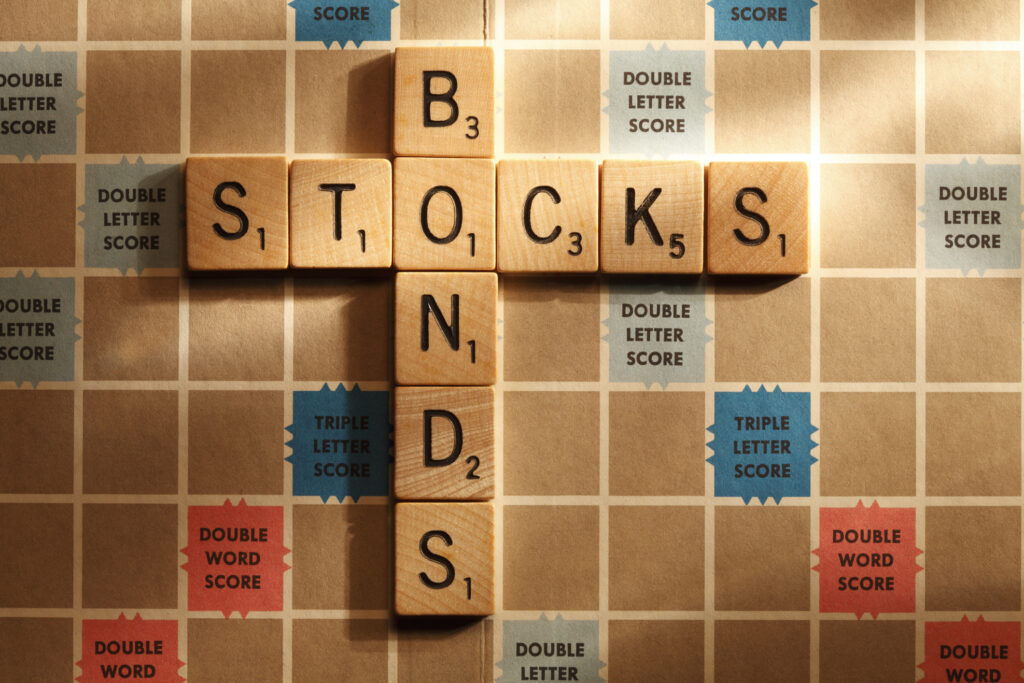 The words "stocks" and "bonds" spelled out on a Scrabble board and connected by the letter "o"