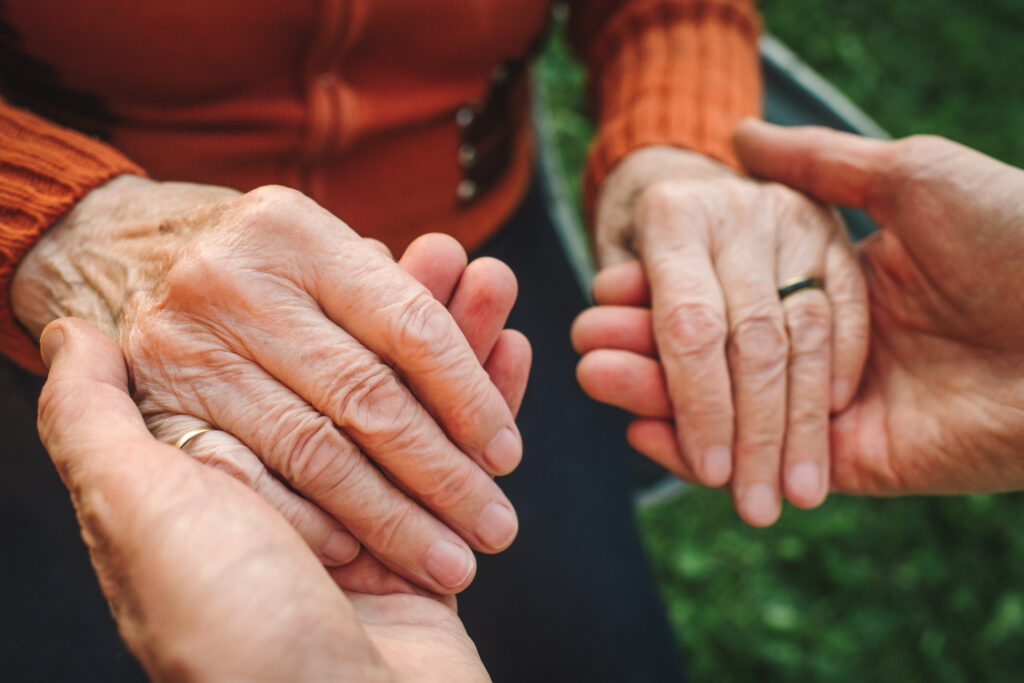 Close-up of a man holding an elderly woman's hands.
