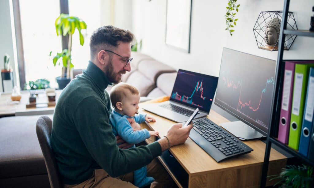 Person with baby looking at financial performance on computer in home office.