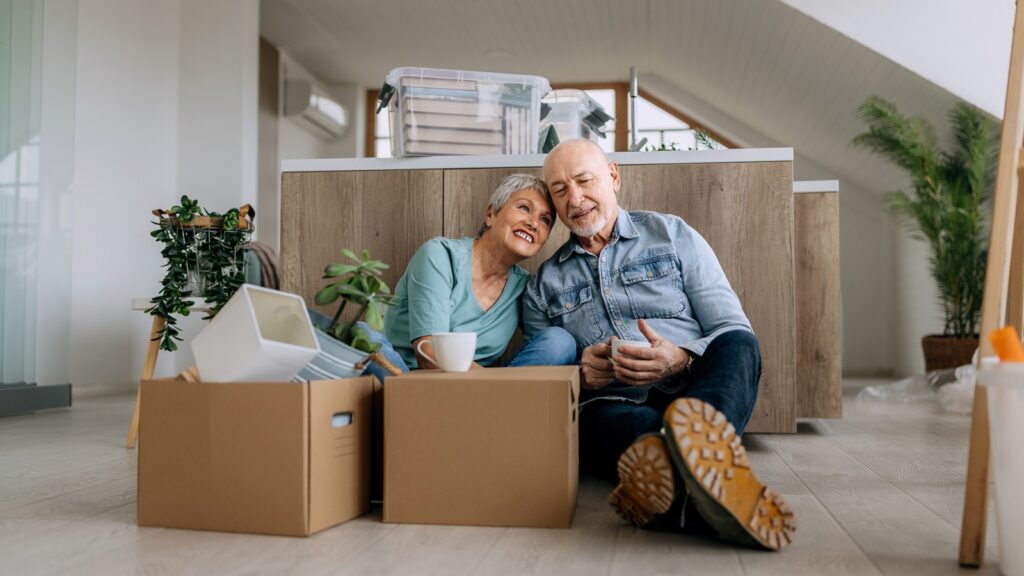 A senior couple sitting on the floor with boxes after downsizing in retirement.