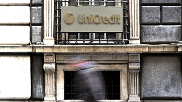 A person walks past a sign with the logo of the Italian bank UniCredit on its bank branch in central Genoa,