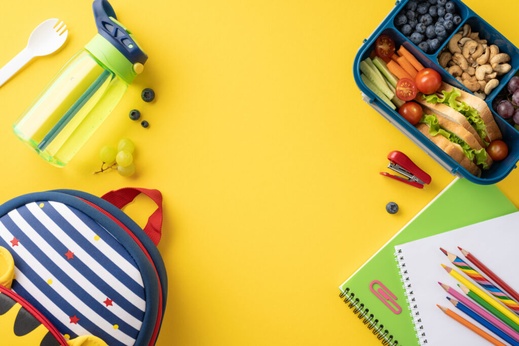 book bag, lunchbox, notebooks, pencils and other school supplies on a yellow background