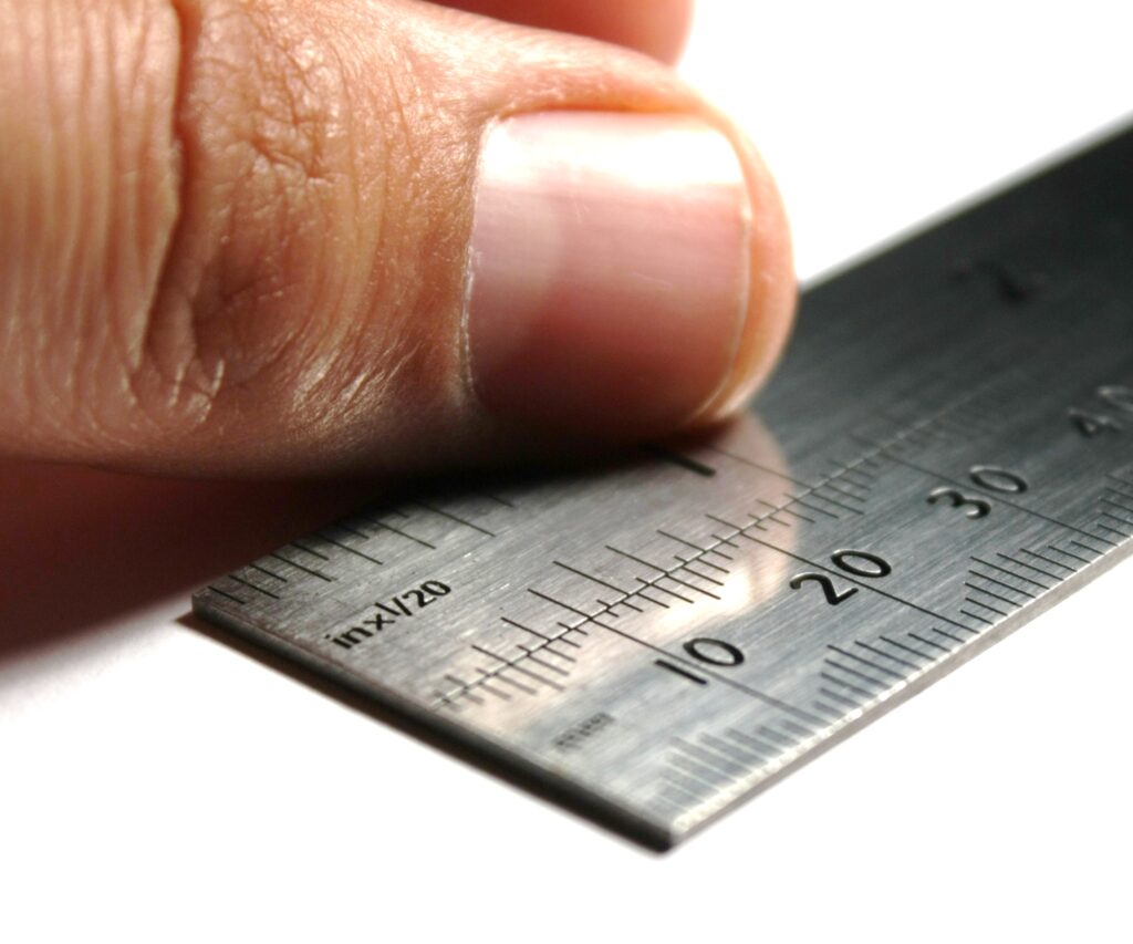 A man's thumb rests on a ruler.