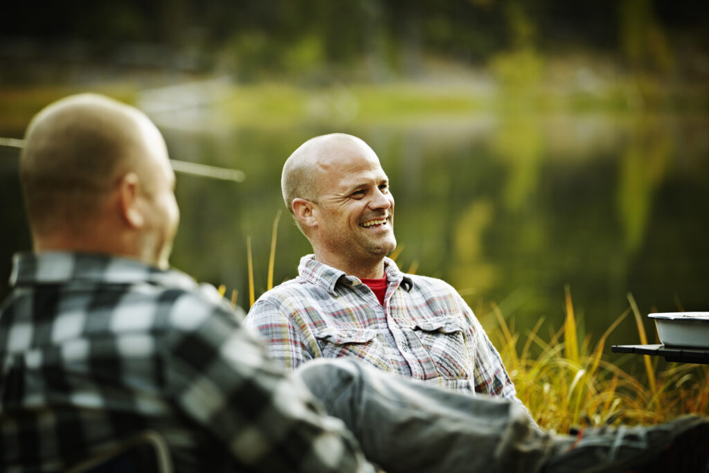 Man sitting in discussion with friends by lake smiling and laughing.