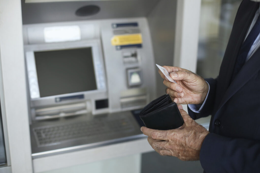 A man pulls a card from his wallet while standing in front of an ATM.