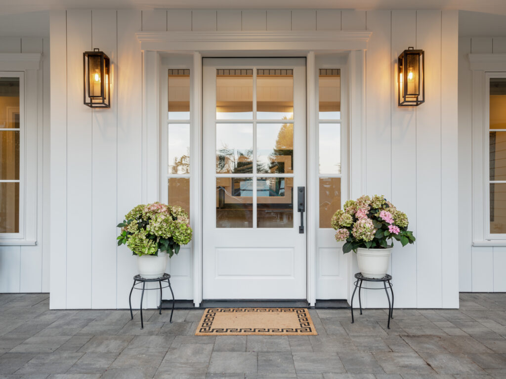 front porch of a house flanked by potted flowers and porch lights