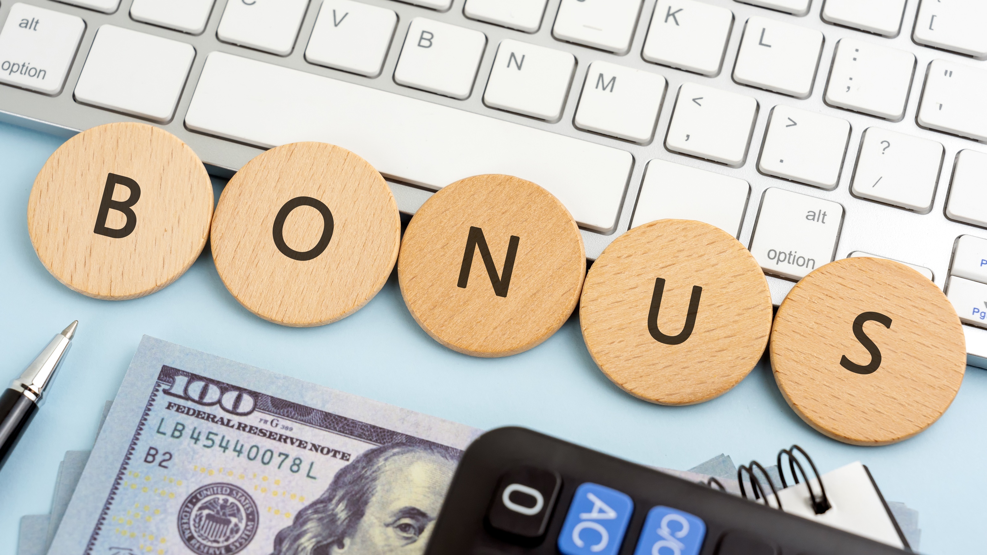 The word "bonus" spelled out on round wooden plates next to a keyboard, money and calculator.