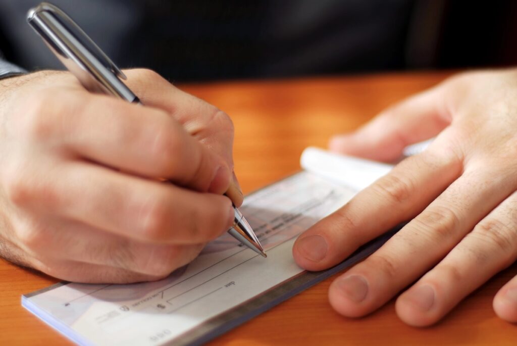 Closeup on man`s hands writing a check to pay off his student loans
