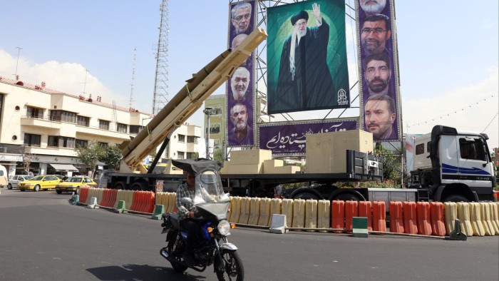 A man rides a motorbike past a Kheibar-Shekan missile displayed next to a large picture of Ayatollah Ali Khamenei in Tehran.