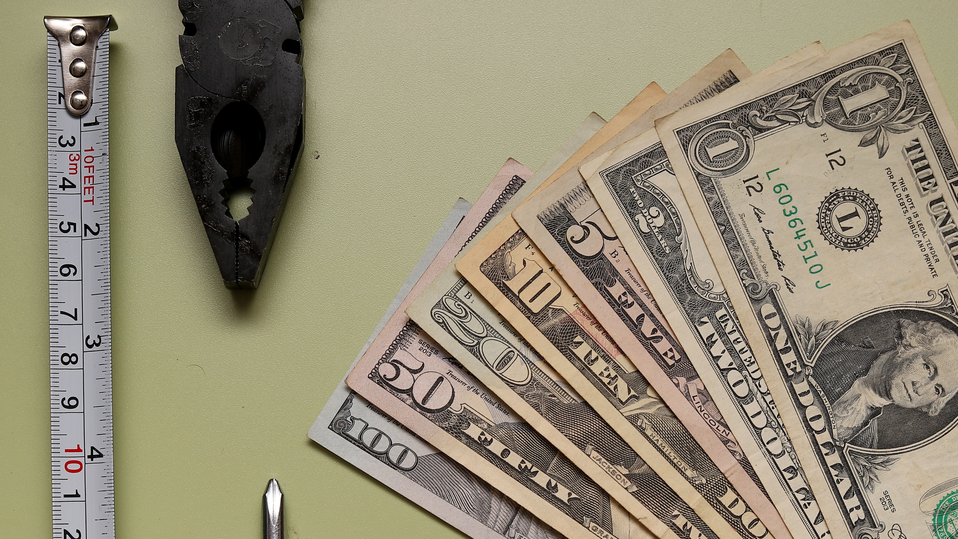 A tape measure and pliers next to fanned-out cash.