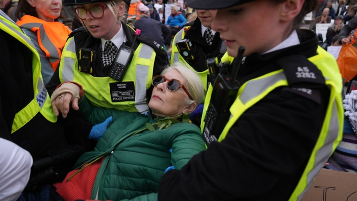 Police officers remove a woman in sunglasses and a green jacket during a protest in Trafalgar Square.