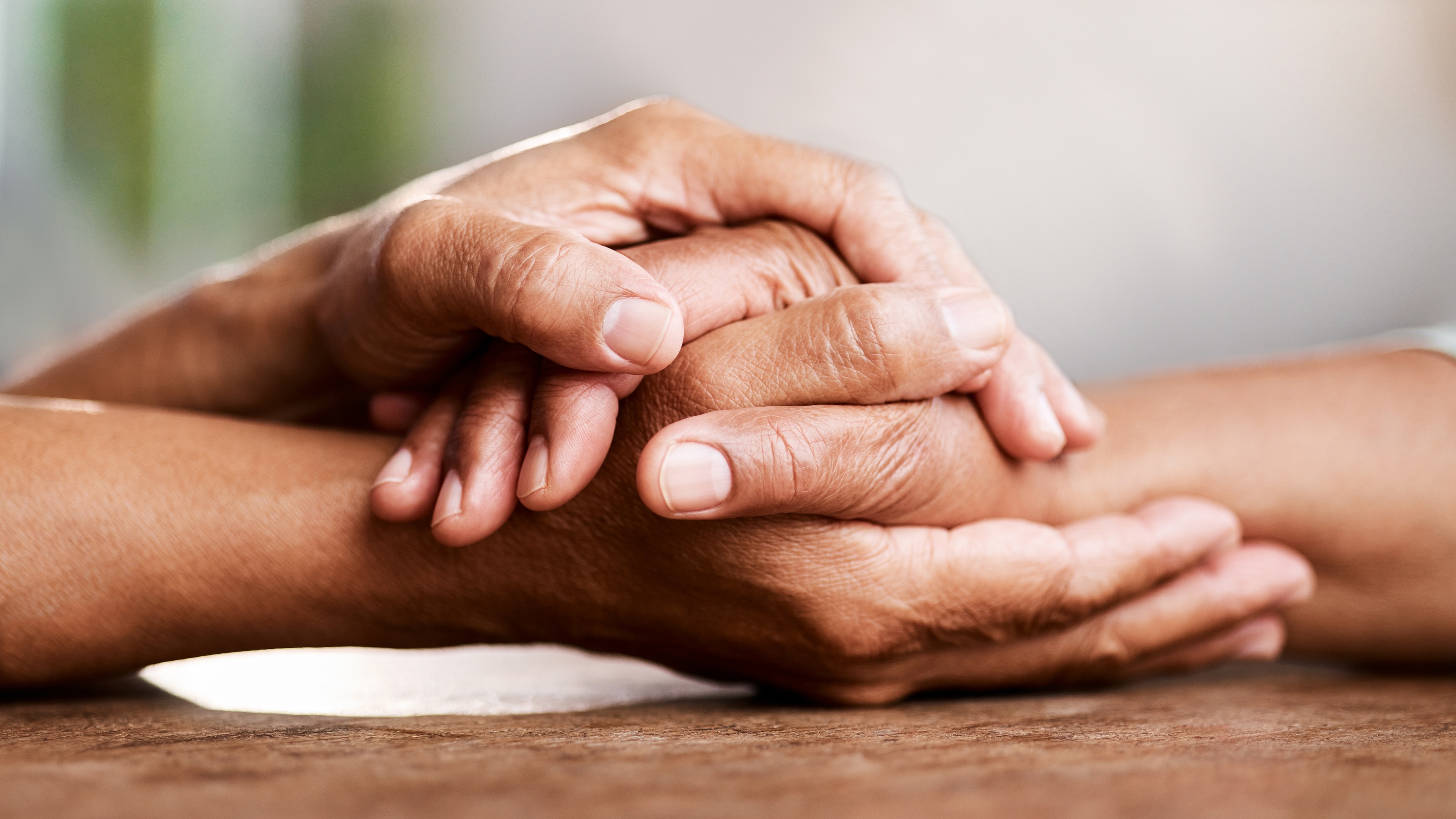 An older couple hold hands on a table, only their hands showing.
