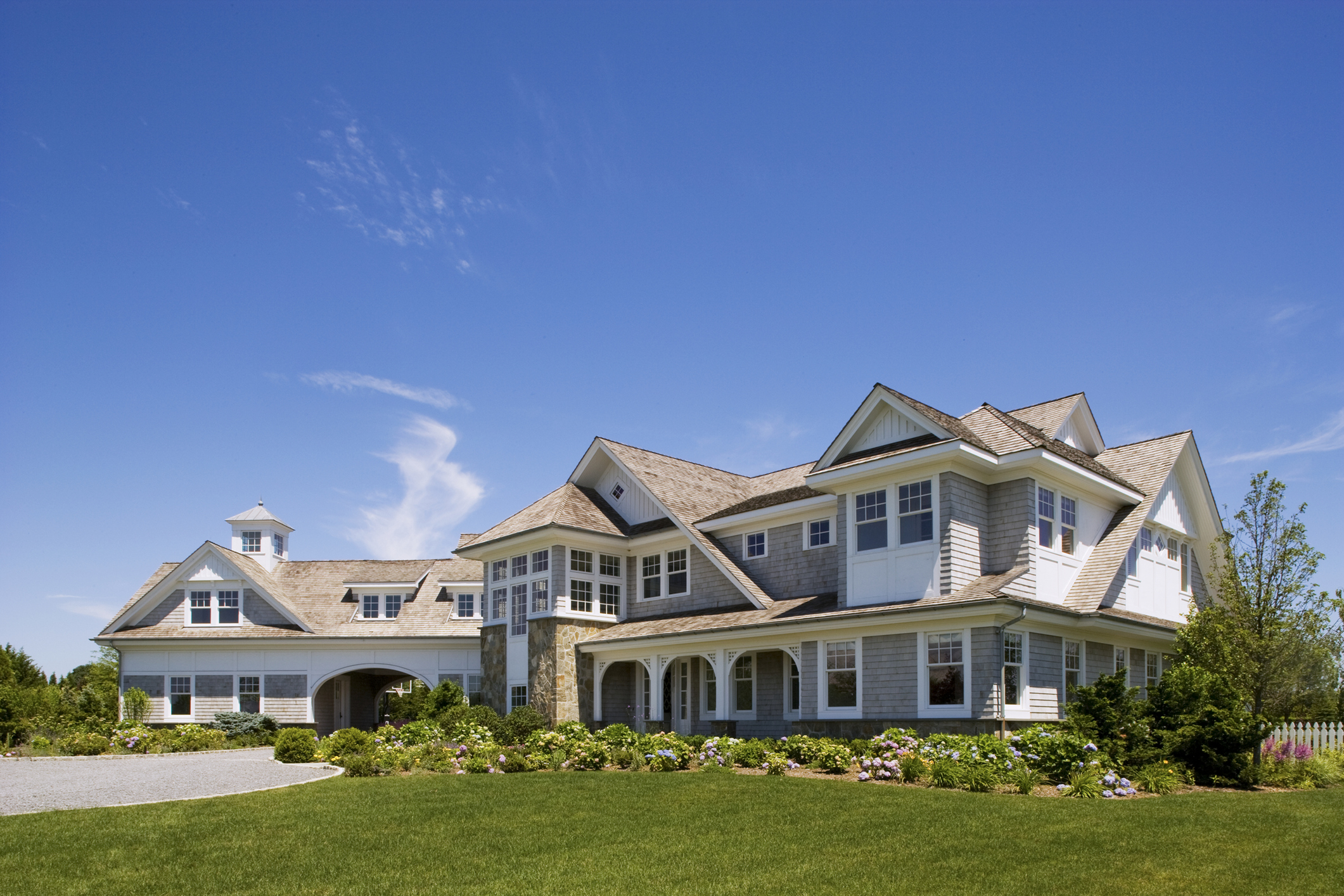 Front exterior of a large private home and estate in the Hampton's on a beautiful summer day.