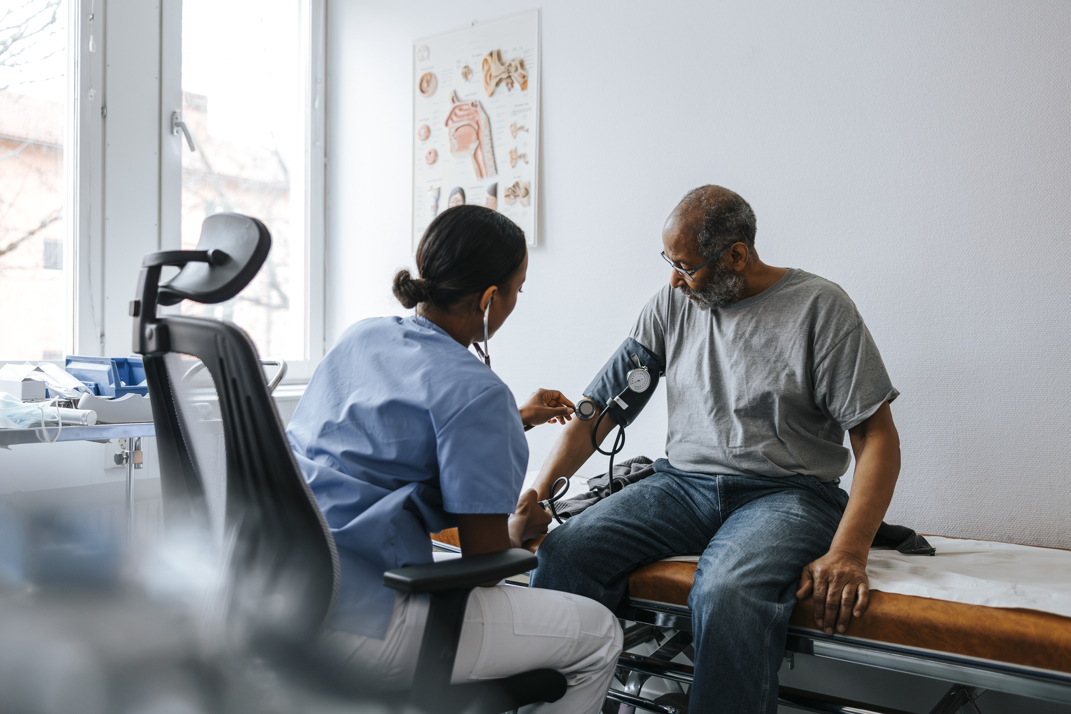 Female doctor checking senior patient's blood pressure sitting on bed in examination room at hospital