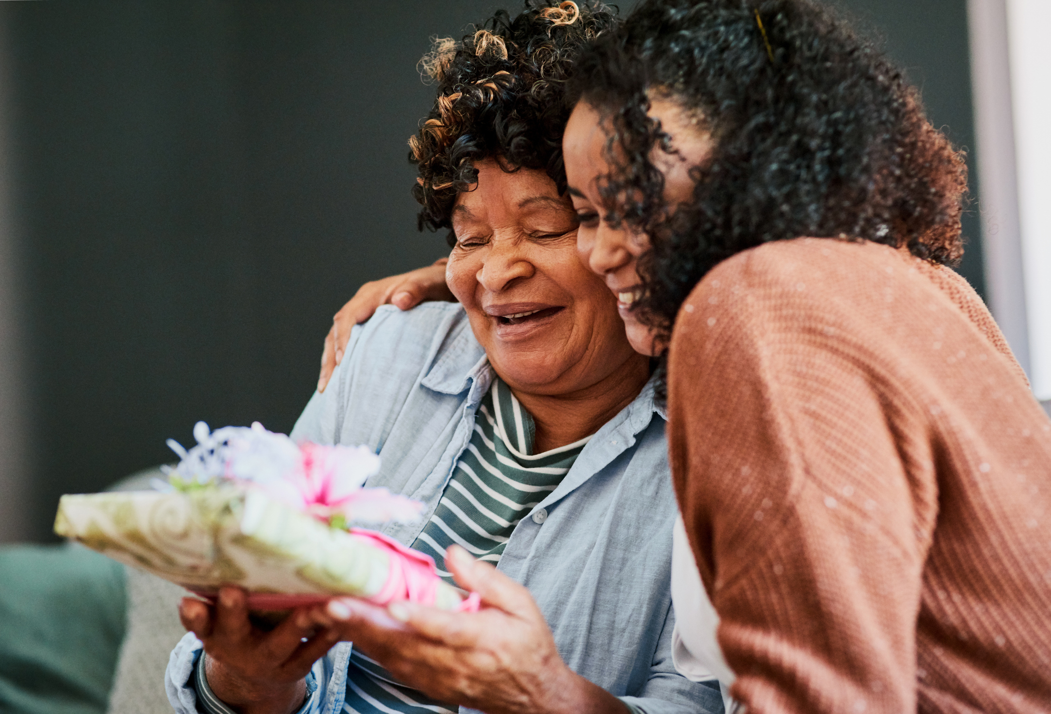 A daughter presents her mother with a wrapped gift.