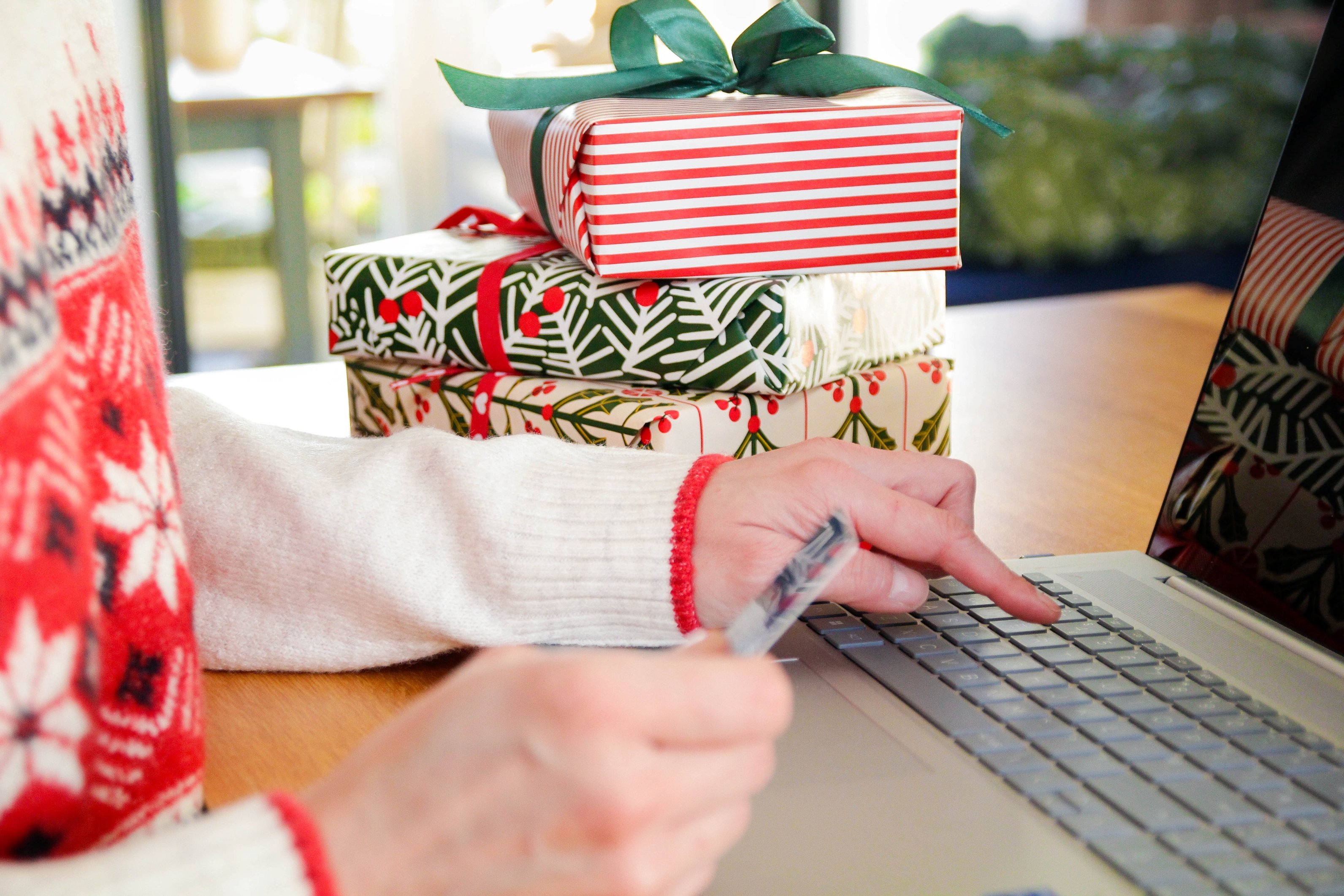 A woman with wrapped Christmas presents beside her types her credit card information into a laptop.