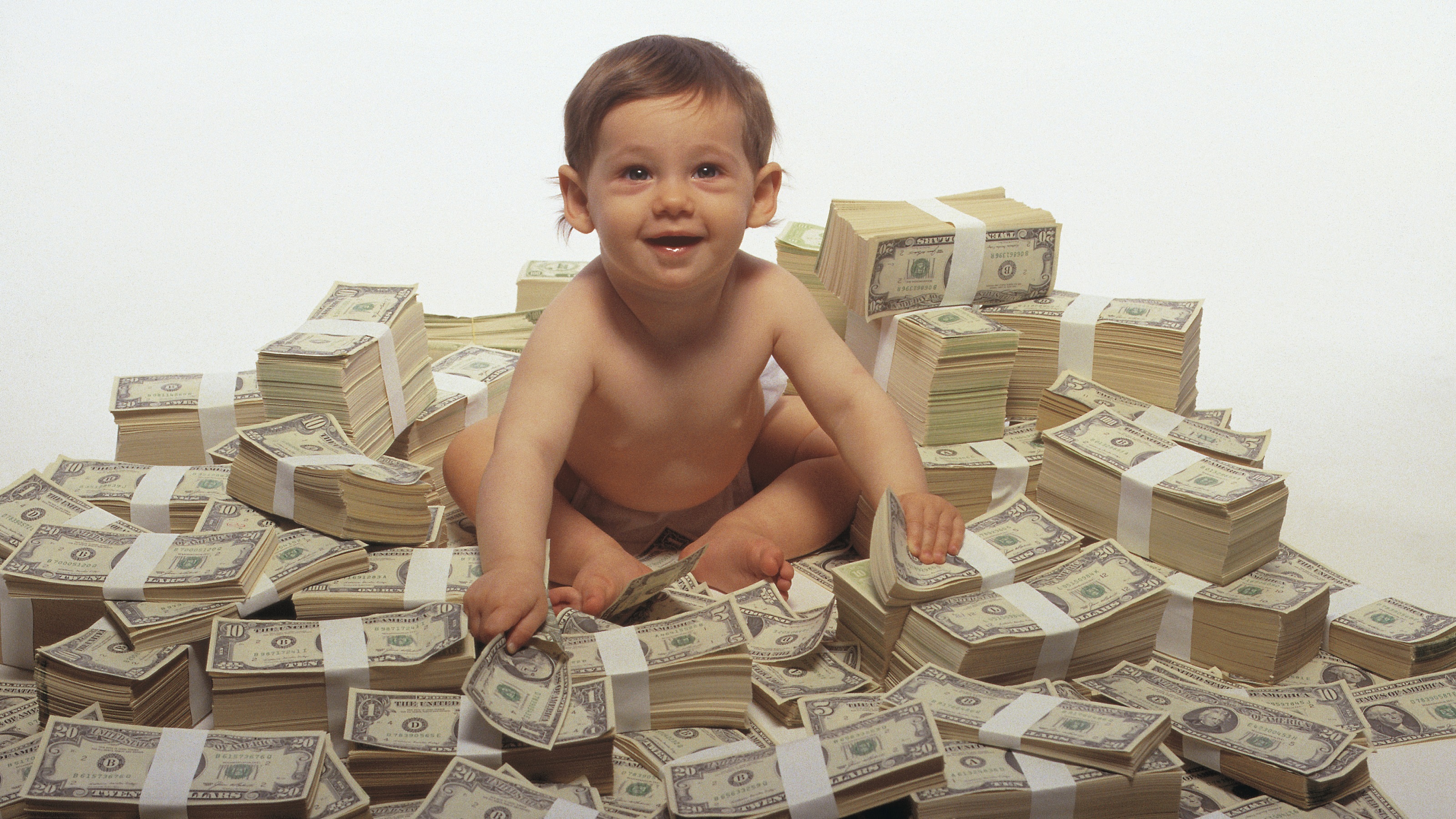 A smiling baby sits atop a pile of cash.