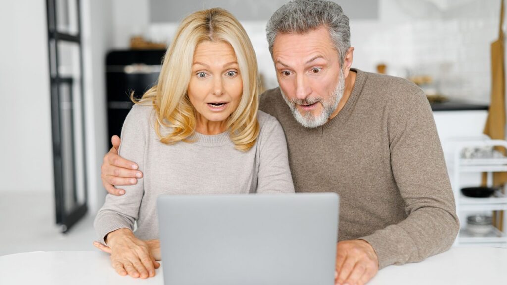 Surprised middle-age couple received unexpected news, mature husband and wife staring at the laptop screen with mouths open and astonished faces expression